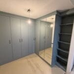 Grey fitted bedroom wardrobes line the walls, with mirrored doors, open shelving and a pale marble-effect floor.