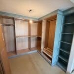 Open fitted dressing room with wood-effect wardrobes, glass-front shelving, drawers and a spacious beige carpeted floor