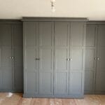 Grey fitted bedroom wardrobes with raised-panel doors, matching cornice and square handles spanning three walls.