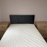 Neatly made double bed with a dark upholstered headboard, white bedding and matching wooden bedside tables in a bedroom