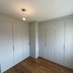 A calm bedroom features floor-to-ceiling grey fitted wardrobes arranged in an L shape, with warm wood flooring.
