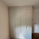 White four-door fitted wardrobe with slim handles, cornice detailing and sunlight casting striped shadows across the doors.