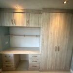 Light oak fitted bedroom furniture with a desk, drawers, overhead cupboards, shelving and a tall double-door wardrobe