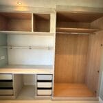 Light wood fitted bedroom storage with open wardrobes, overhead cupboards, shelving, drawers and a continuous desk surface
